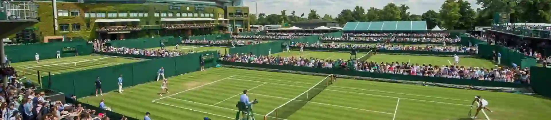 Crowds watching tennis matches on the grass courts at Wimbledon under a blue sky