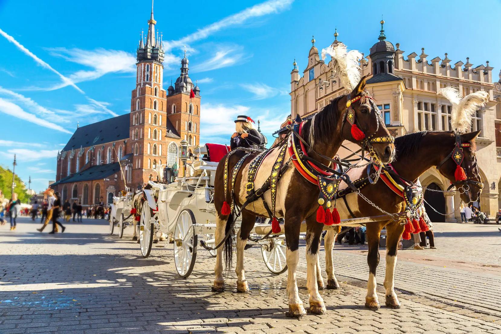 Traditional horse and carriage in Kraków, Poland, standing near St Mary’s Church in the Market Square, with the church’s gothic towers and surrounding historic buildings visible
