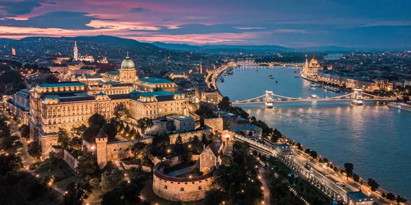 High angle view of the city of Pest at night time, showing its lit up buildings, the Danube river, and some of Pest