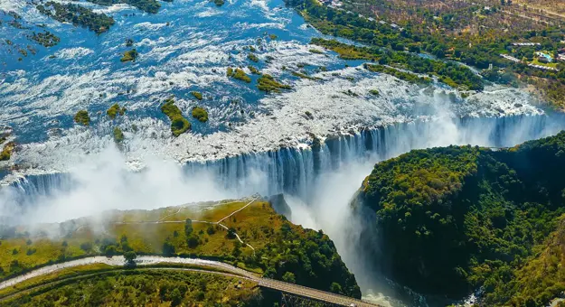 Aerial view of Victoria Falls in Zimbabwe, with water cascading over the cliffs and mist rising above the surrounding landscape
