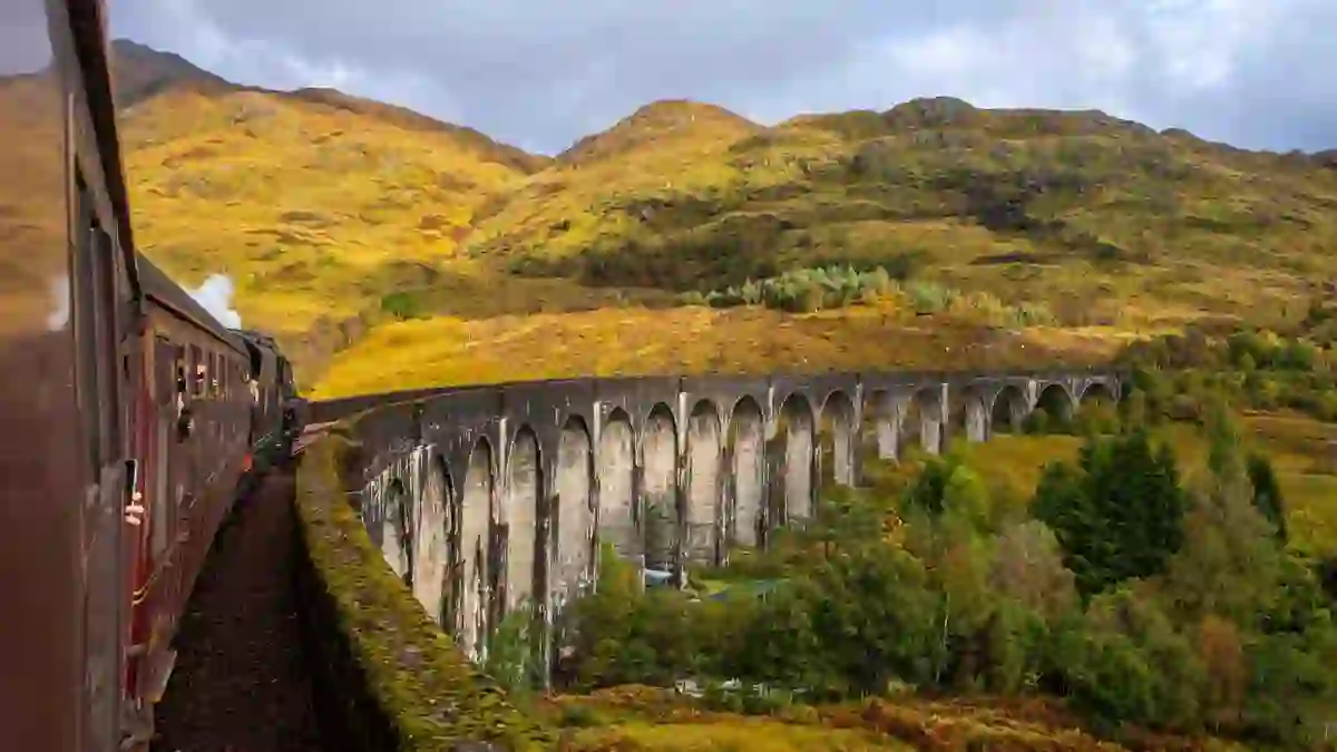 Shot of a steam train going along railway on a viaduct in the highlands from behind 