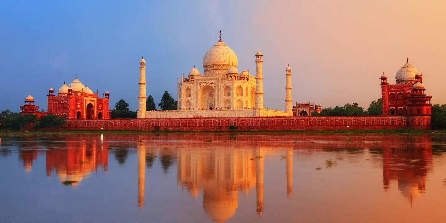 The Taj Mahal in Agra reflected in the calm waters of the Yamuna River at sunset