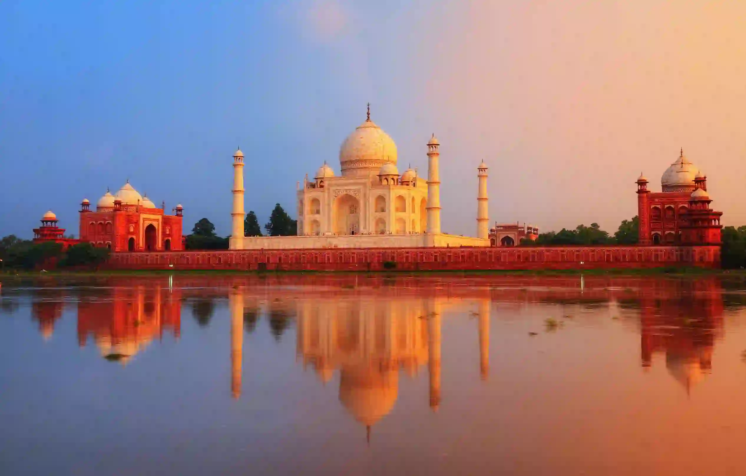 The Taj Mahal in Agra reflected in the calm waters of the Yamuna River at sunset