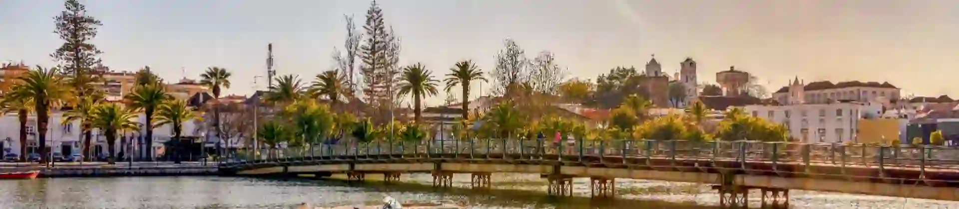 Two small boats moored in front of a bridge in Tavira on the Algarve, with trees and buildings lining the water’s edge in the background