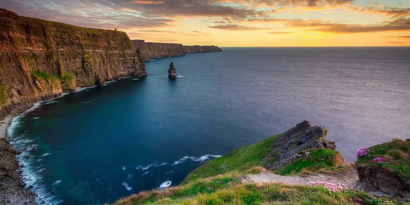 High angle shot of a coast line, with cliffs that curve to the right and rocky land in the right forefront