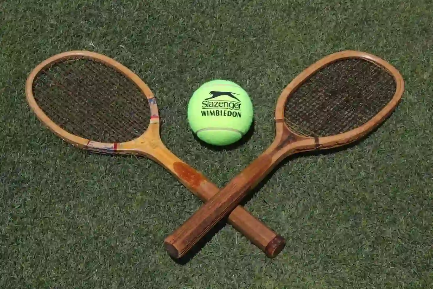 Two wooden tennis rackets and a yellow Slazenger tennis ball arranged on a green lawn