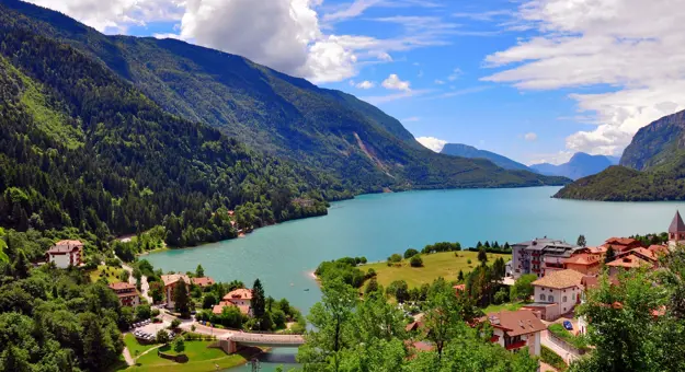 Shot of Molveno Lake in Italy, with buildings in the forefront and mountains 