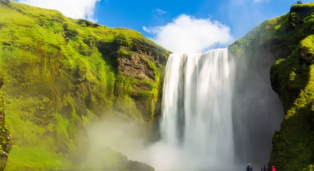 Waterfall surrounded by mossy rock. Steam coming off the water, people stood below the waterfall.