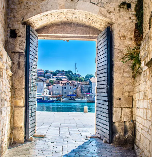 View of a boat on some water, with buildings behind it, through open doors in a stone walkway. A bright blue sky.