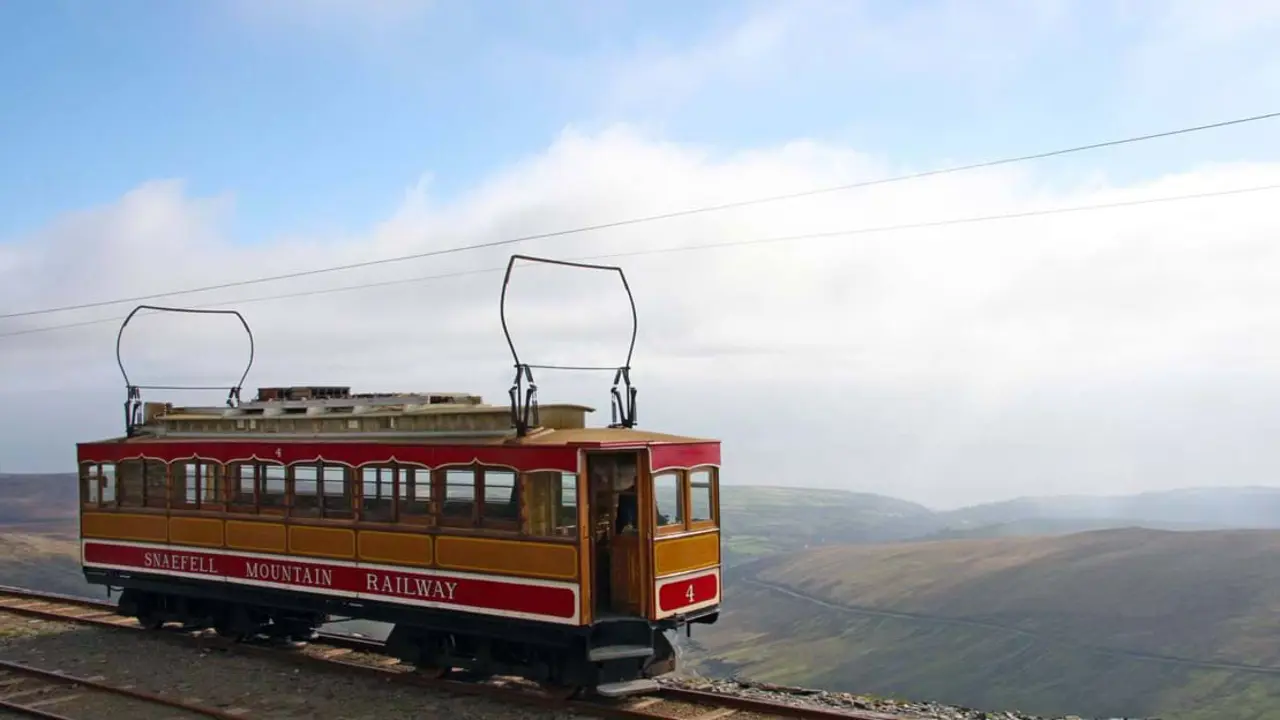 'Snaefell Mountain Railway' electric train travelling on the side of a mountain, with clouds and mountains behind it 