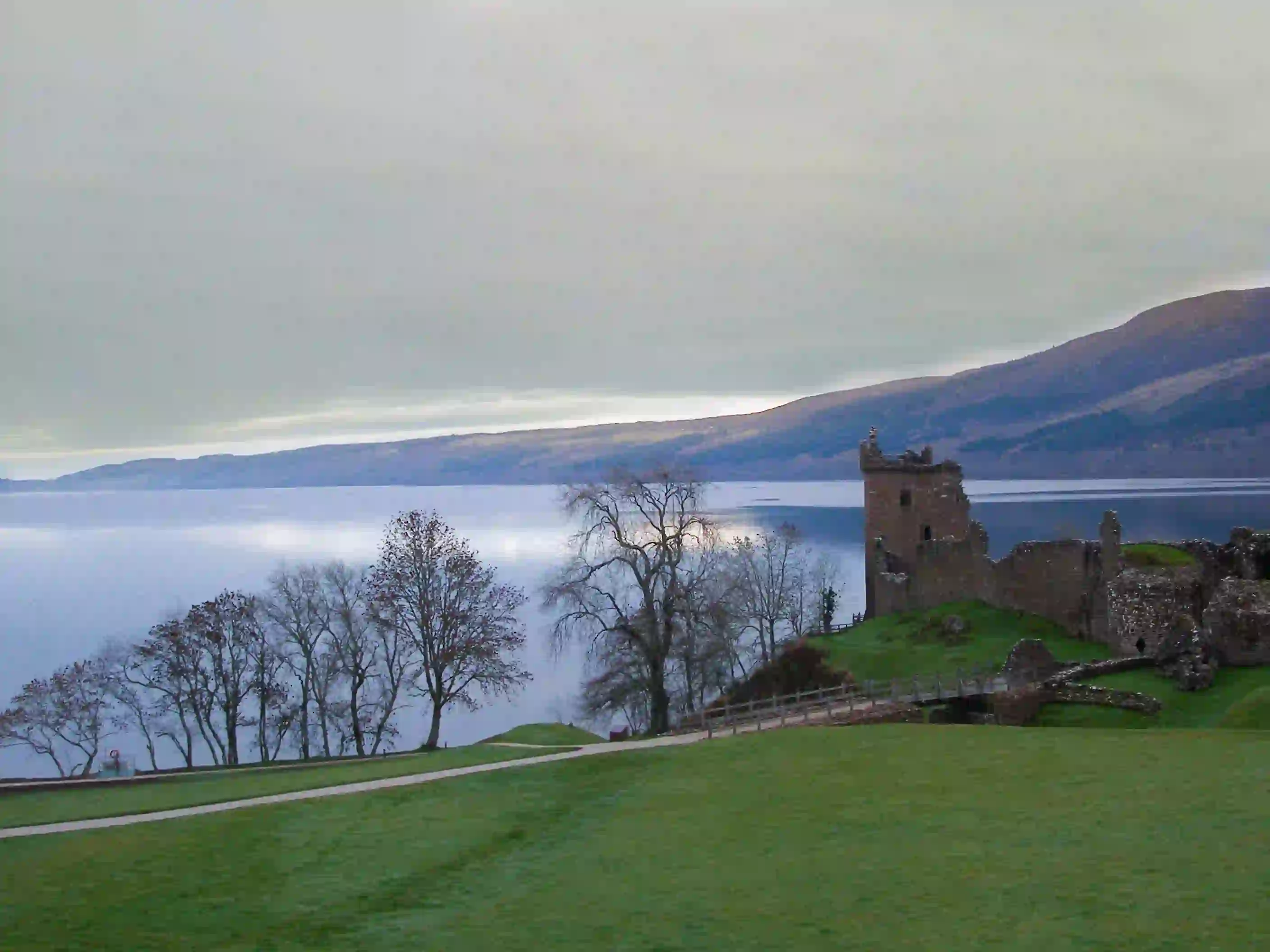 Urquhart Castle overlooking Loch Ness, with grass and leaveless trees in the forefront