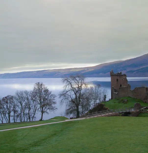 Urquhart Castle overlooking Loch Ness, with grass and leaveless trees in the forefront