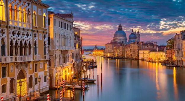 Sunset view of Venice featuring the iconic Salute Church beside a winding canal that stretches toward the open sea