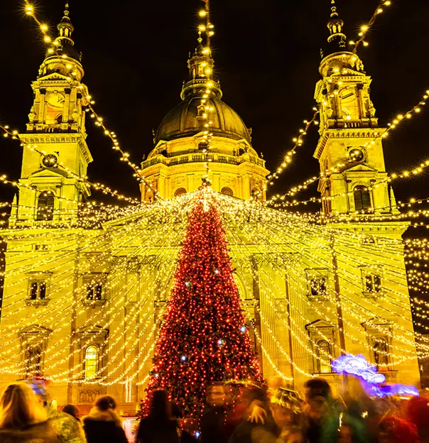 Low angle shot of a large christmas tree covered in red lights, with gold fairy lights strung out of it. Lit up St. Stephen's Basilica behind it.