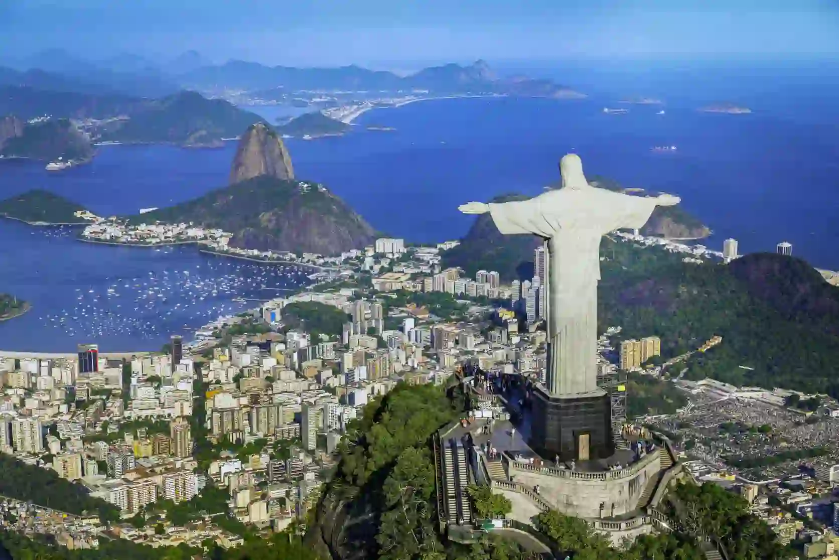 Panoramic view of Rio de Janeiro with Sugarloaf Mountain, the Christ the Redeemer statue, and city buildings along the coastline