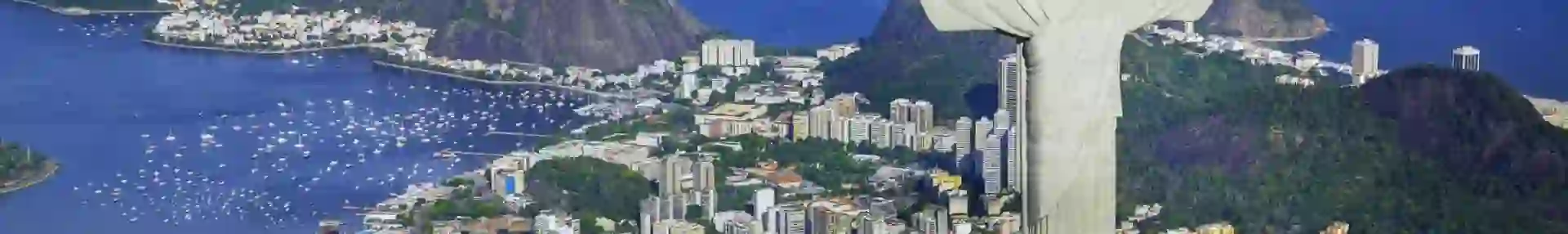 Panoramic view of Rio de Janeiro with Sugarloaf Mountain, the Christ the Redeemer statue, and city buildings along the coastline