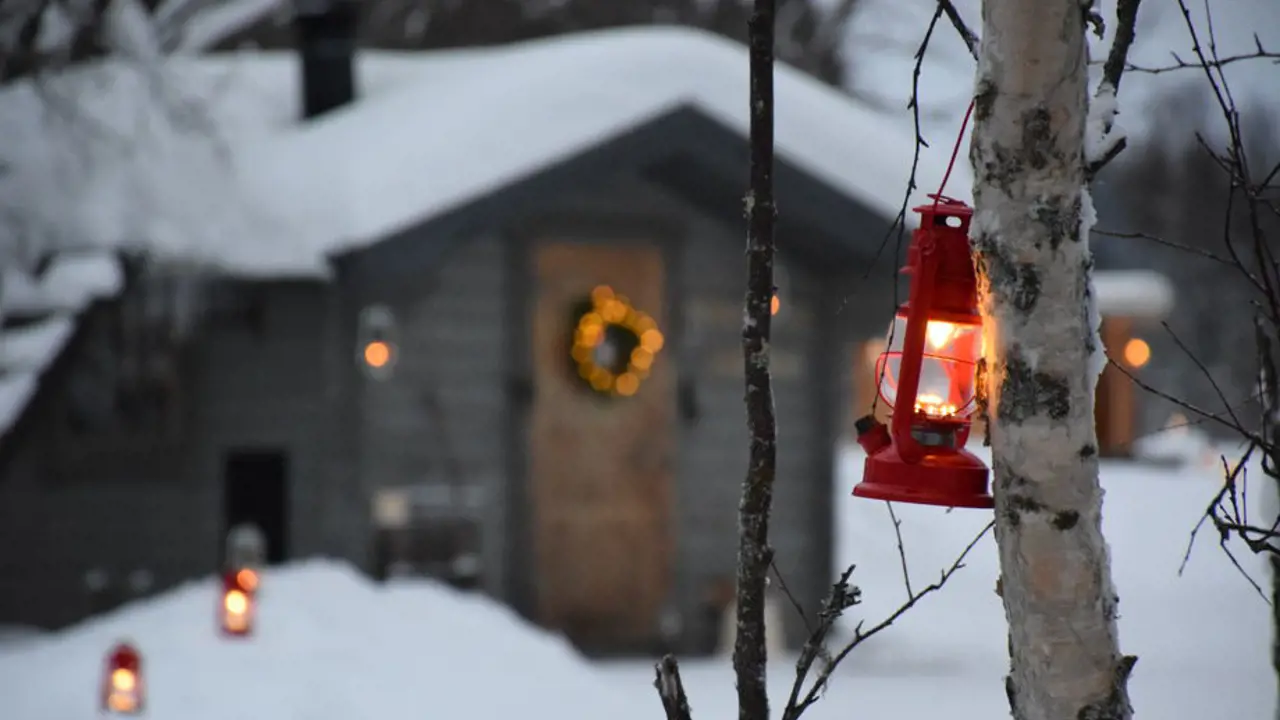 Close up of a lantern tied to a tree with Santa's Grotto in the background, in the snowy woods