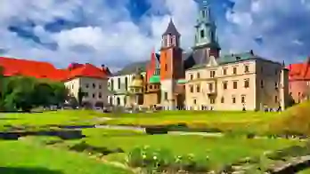 Wawel Castle in Kraków, Poland, showcasing its historic towers and red-brick walls beneath a cloudy blue sky