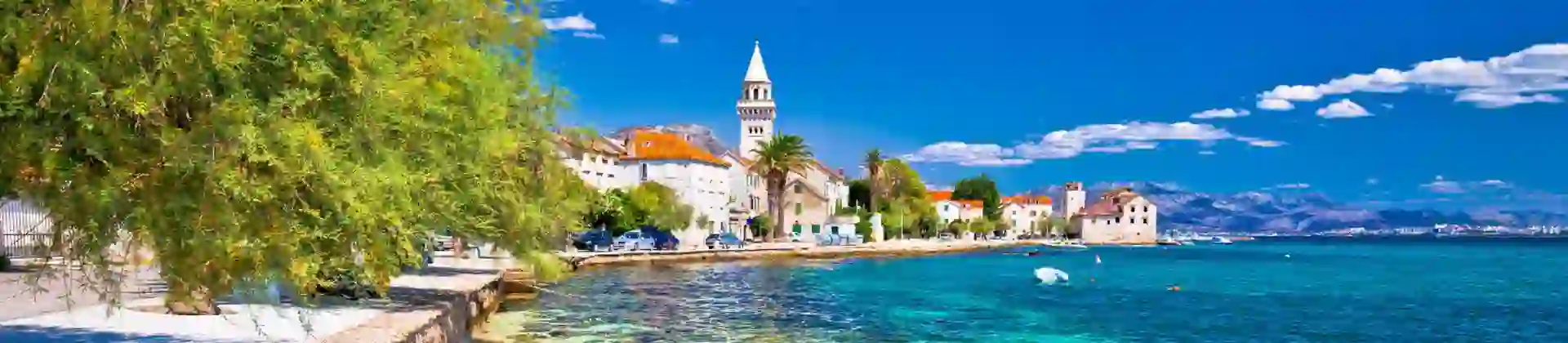 Scenic coastal view of Kaštel Štafilić near Split, Croatia, with crystal-clear turquoise water, stone buildings, and a church bell tower in the distance