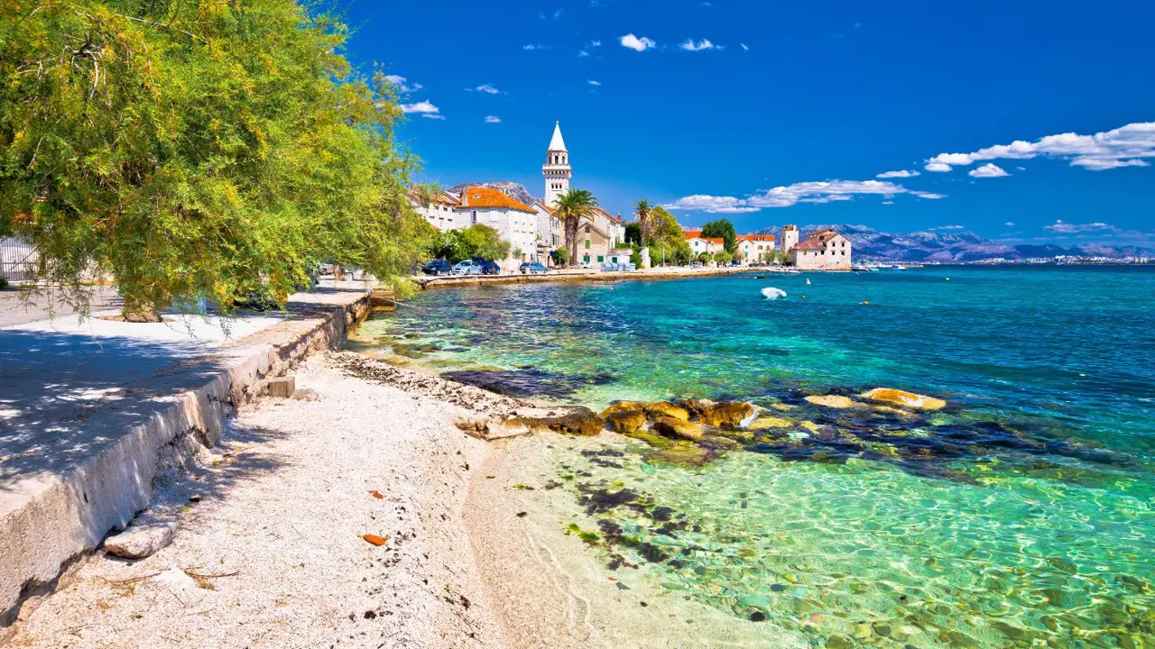 Scenic coastal view of Kaštel Štafilić near Split, Croatia, with crystal-clear turquoise water, stone buildings, and a church bell tower in the distance