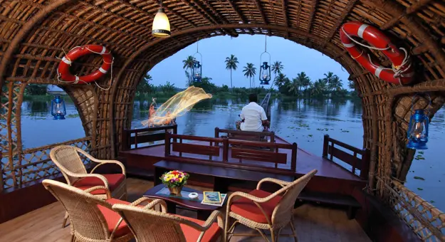 View from the lounge area of a Kerala houseboat sailing on the river, showing calm waters, lush greenery, and palm trees along the banks