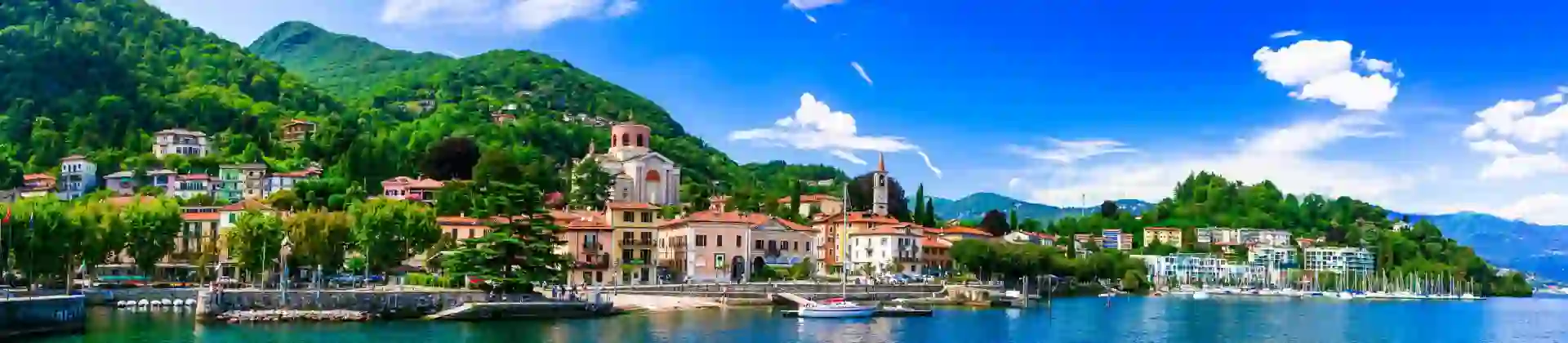 Lake Maggiore in Italy, with an Italian town on the shore beneath a bright, partly cloudy sky