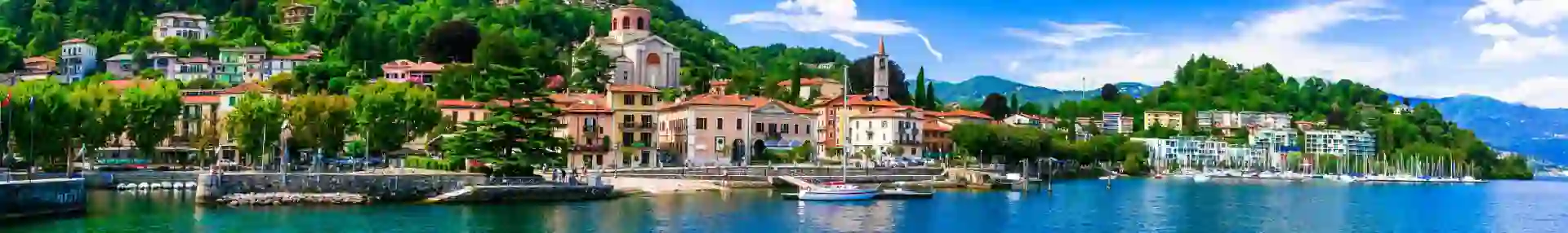 Lake Maggiore in Italy, with an Italian town on the shore beneath a bright, partly cloudy sky