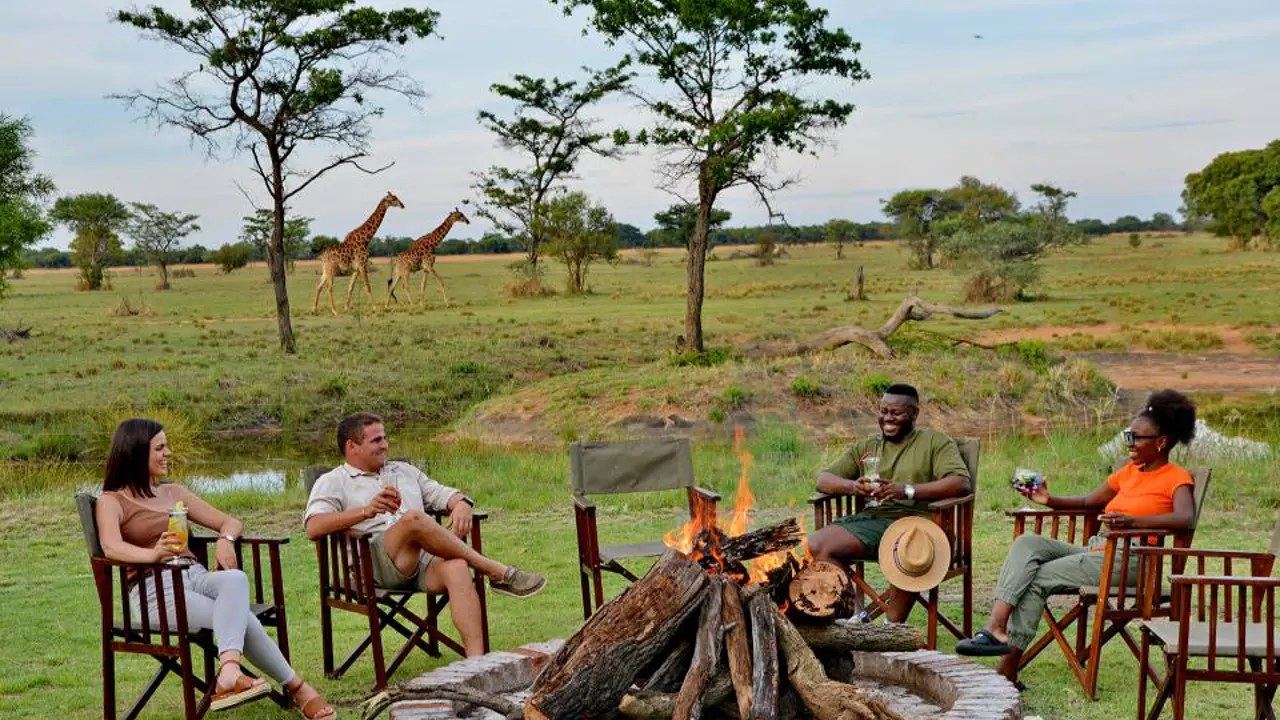 Guests sitting around the fire pit with giraffes in the distance