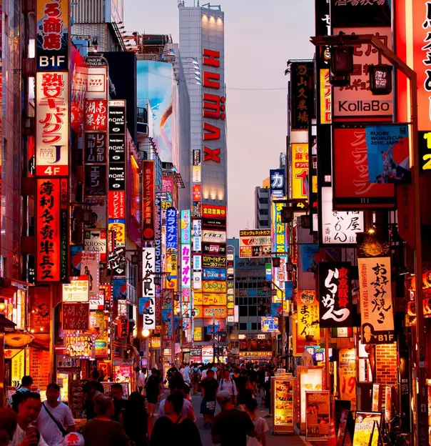 bustling cityscape of Tokyo at dusk, featuring bright lights, high-rise buildings, and busy streets filled with cars and pedestrians