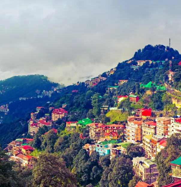 A panoramic view of Shimla’s colourful hillside buildings surrounded by green mountains and misty clouds in the Himalayan foothills