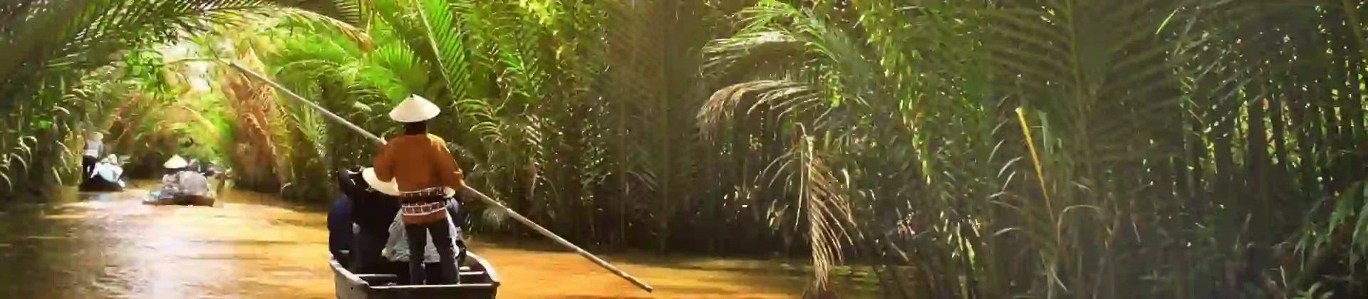 Small wooden boats glide through a palm-lined canal off the Mekong River in Thailand, with a person in a conical hat steering under filtered sunlight