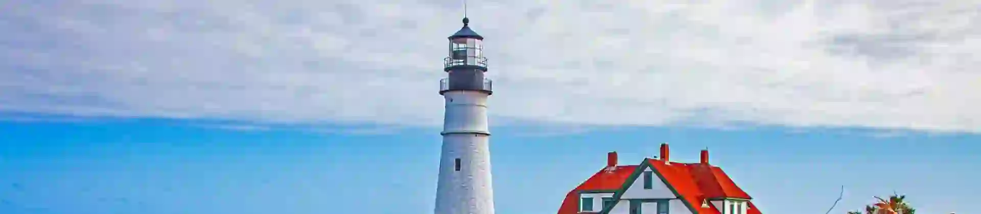 White lighthouse and red-roofed buildings on a rocky coast in Portland, with autumn foliage in the foreground