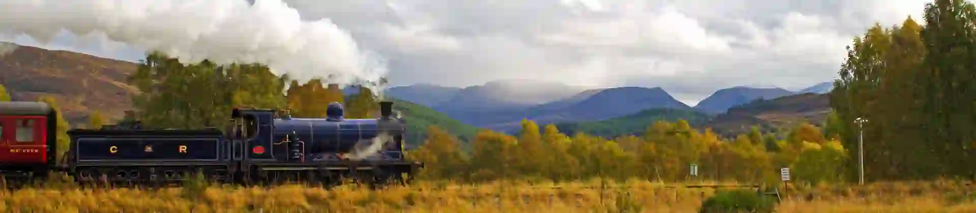 Steam train approaches Kinchurdy Bridge against Cairngorms