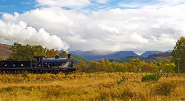 Steam train approaches Kinchurdy Bridge against Cairngorms