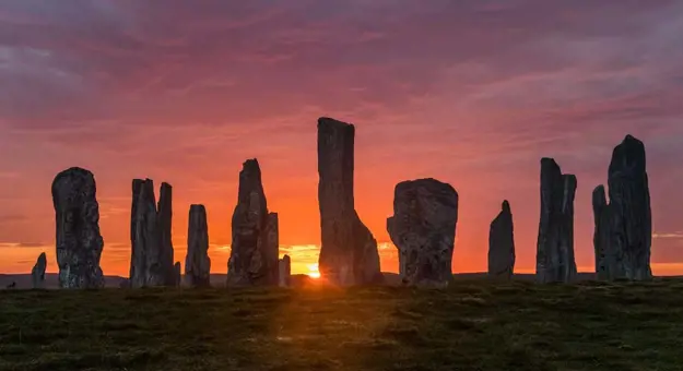 Silhouette of Calanais Standing Stones, with the sun rising behind them 