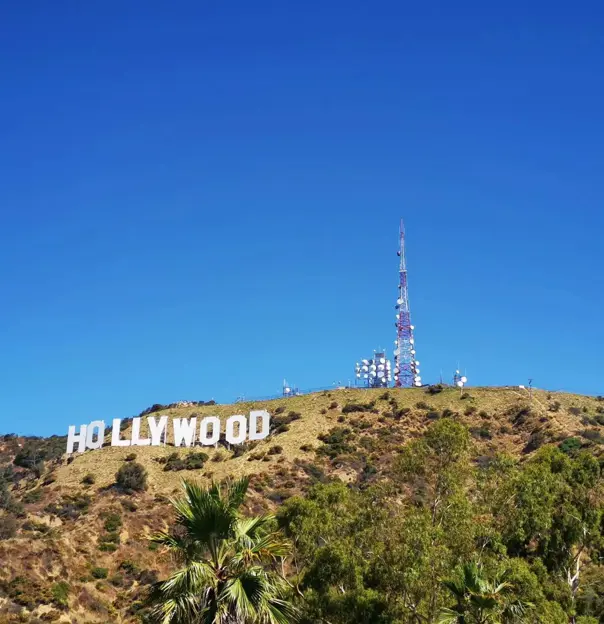 View of the iconic Hollywood sign on a hillside in Los Angeles, with clear blue sky and surrounding greenery