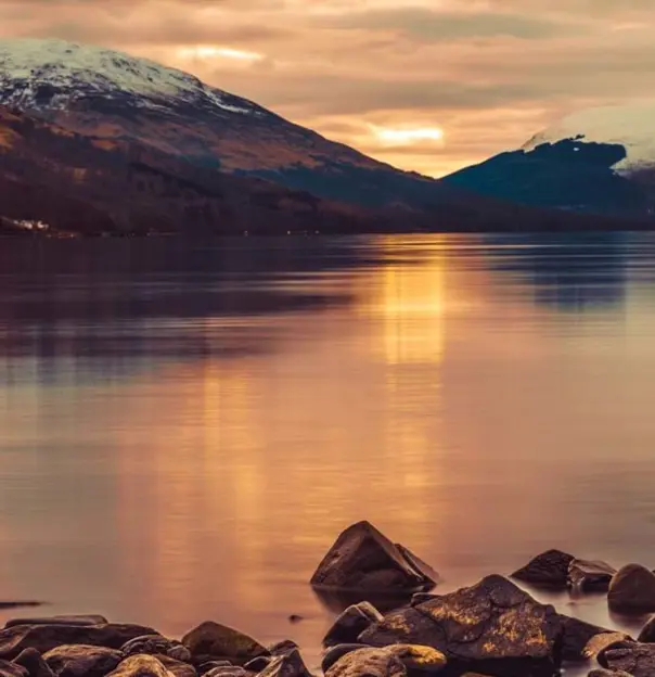 Loch Lomond at sunset, with snowy mountains in the distance