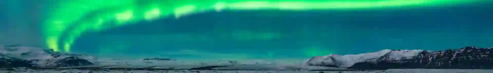 Green northern lights curving from the right back to the left. Below, a lake with ice blocks