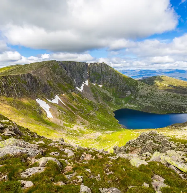 View of Cairngorms National Park, with a small body of water in the centre and a cloudy, but blue sky