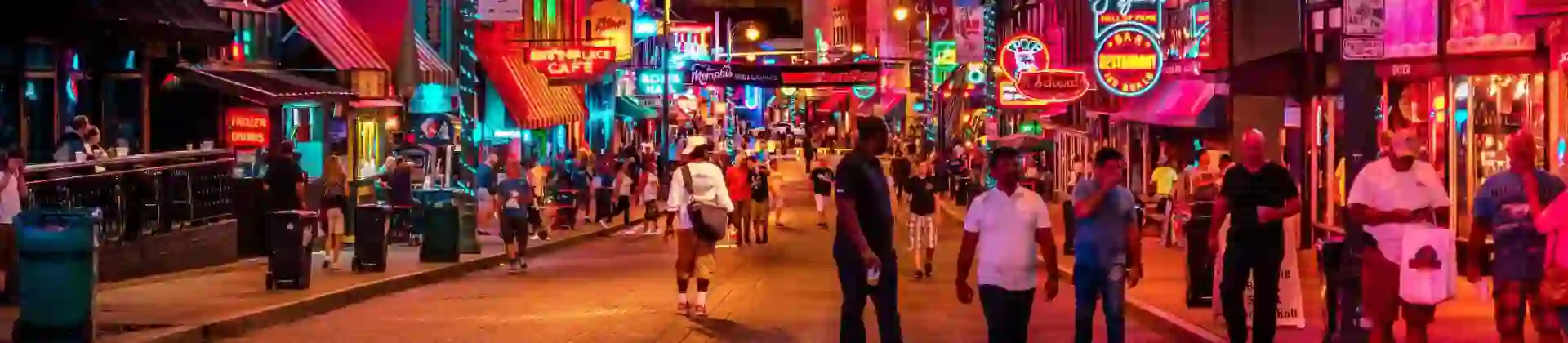 Vibrant night scene on Beale Street in Memphis, with neon signs glowing above blues clubs, bars, and live music venues, and crowds of people walking along the historic street