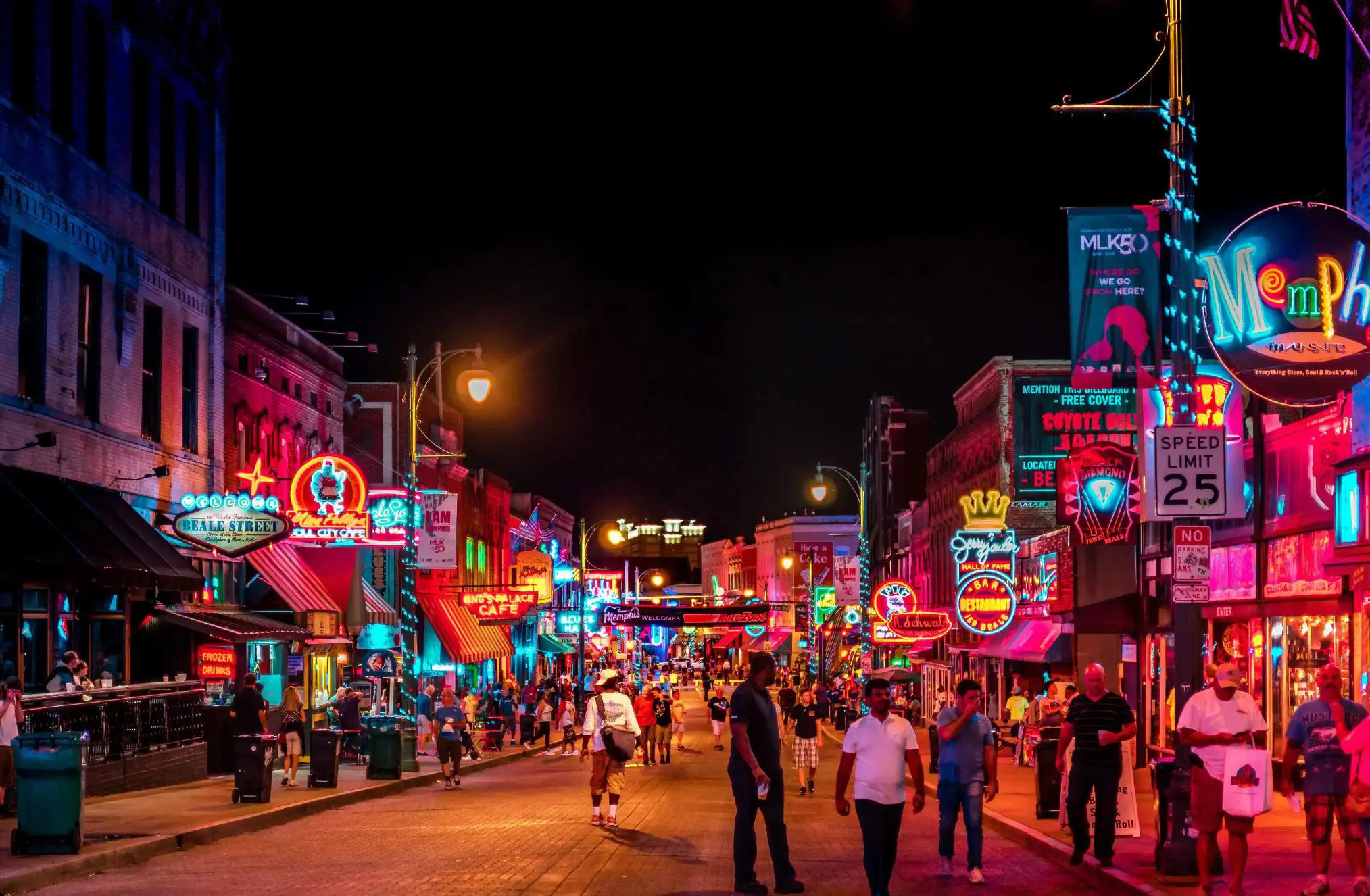 Vibrant night scene on Beale Street in Memphis, with neon signs glowing above blues clubs, bars, and live music venues, and crowds of people walking along the historic street