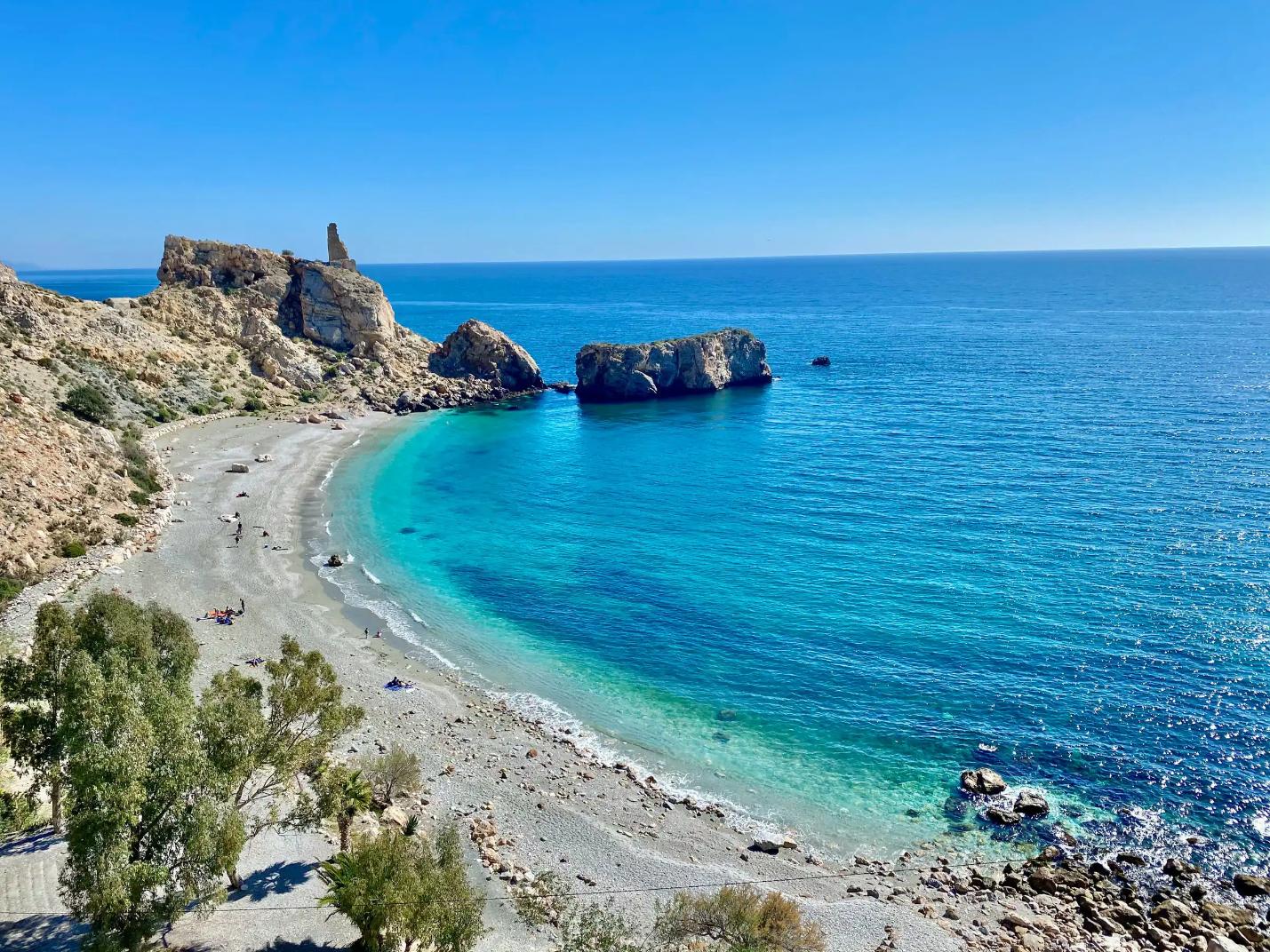 A wide sandy beach along the Costa de la Luz in Andalucía, Spain, with gentle waves lapping the shore under a clear blue sky