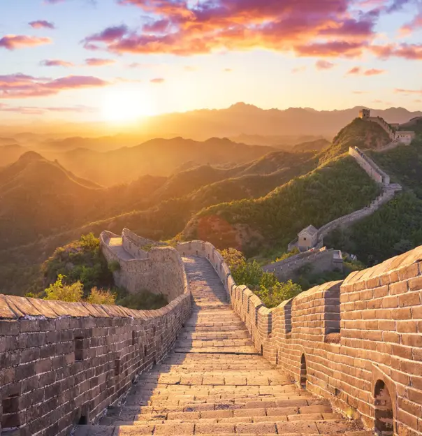 The Great Wall winding over mountain ridges, glowing in golden light at sunset, near Beijing, China
