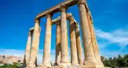 Low angle shot of temple ruins, with pillars. Blue sky behind