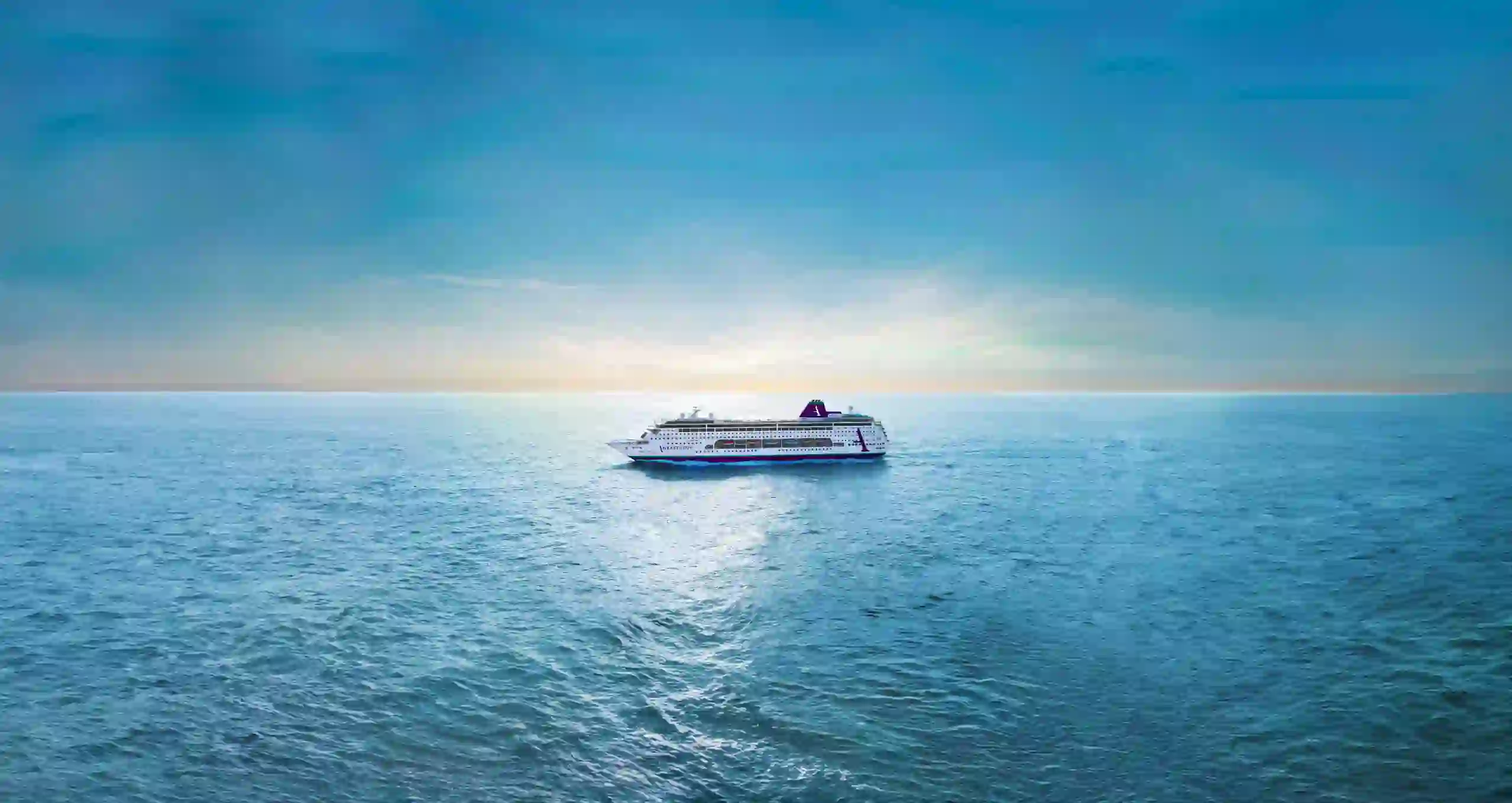 A distant view of the Ambition cruise ship on a calm sea under clear blue skies