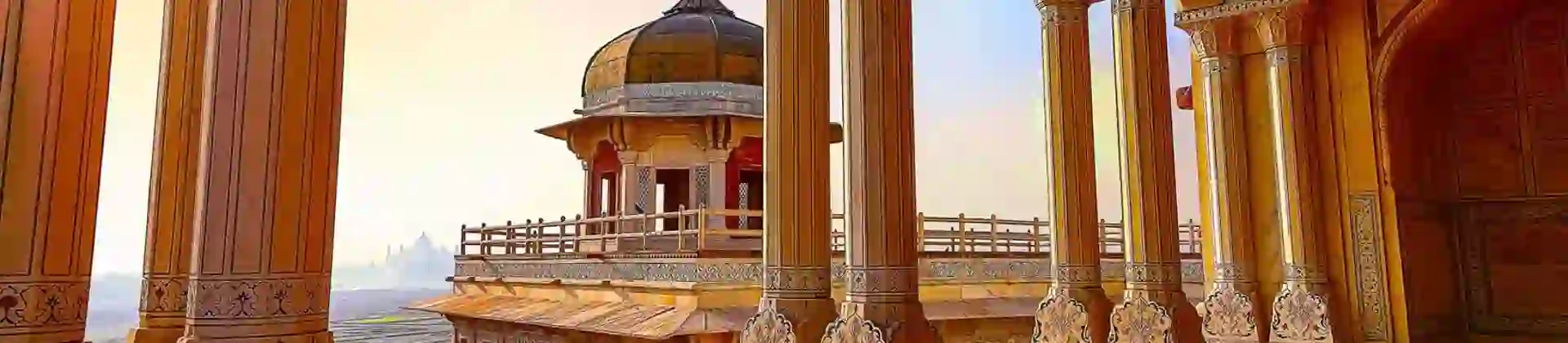A view through ornate sandstone arches at Agra Fort, overlooking a domed pavilion and distant landscape in warm evening light