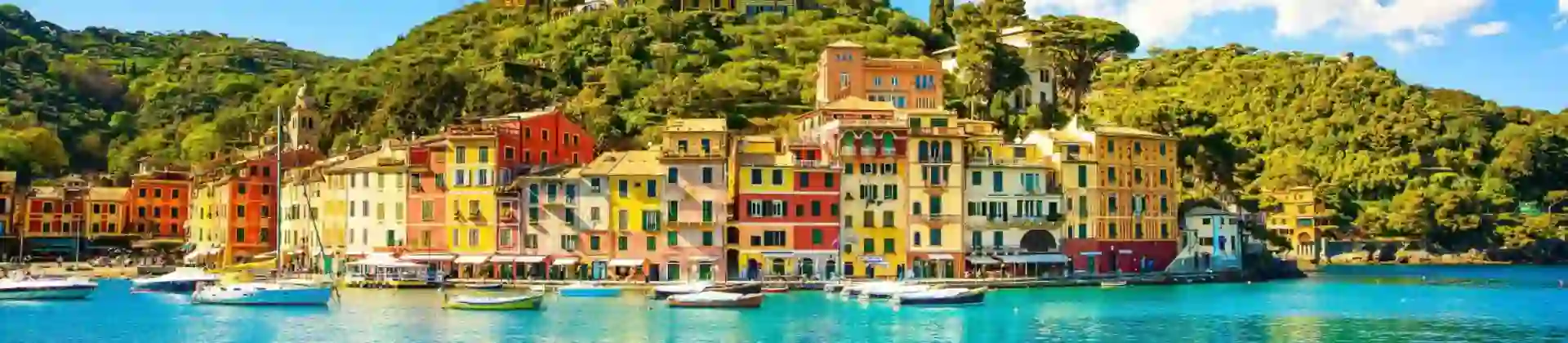 Picturesque view of Portofino, Italy, featuring colourful harbourfront buildings, boats gently floating in the clear blue water, and lush green hills in the background