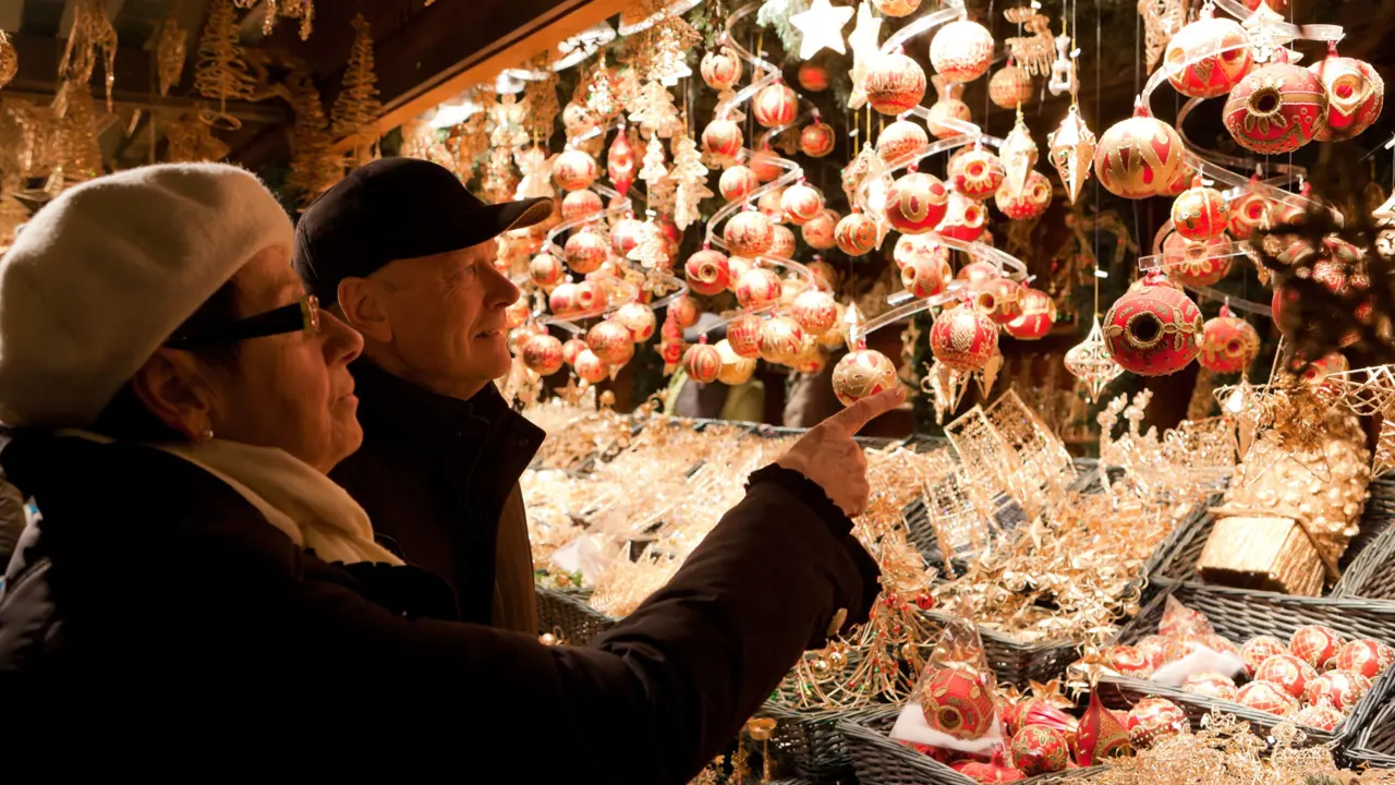 Mature couple looking at Christmas baubles being sold at a Christmas Market stall. The woman, who is in the forefront, is pointing towards one.