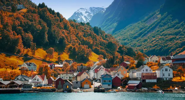 The village of Flam in Autumn, with brown trees going up the mountain and houses on the bay of the water