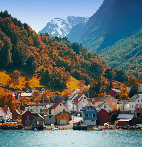 The village of Flam in Autumn, with brown trees going up the mountain and houses on the bay of the water